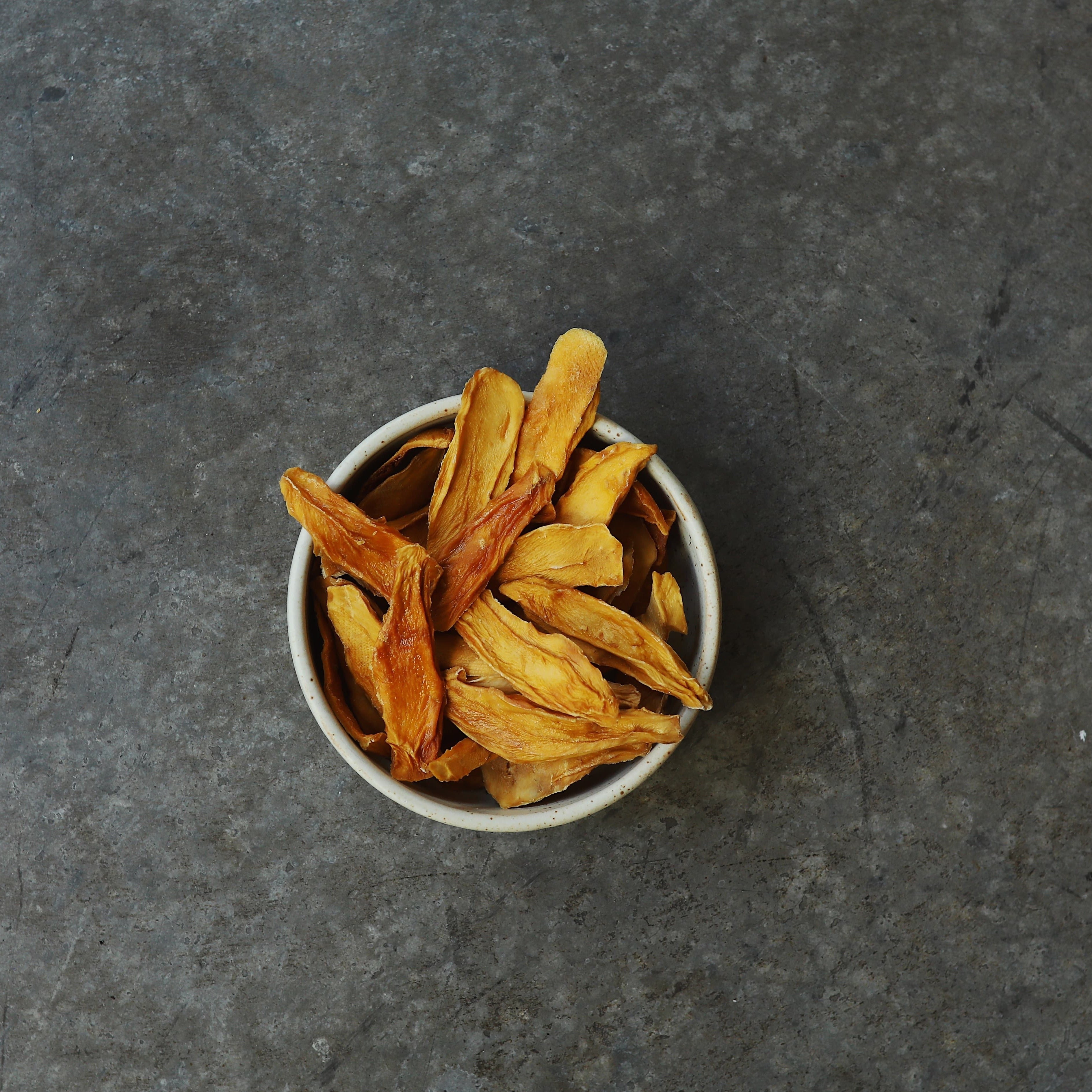 Organic dried mango strips in clay bowl on concrete background.