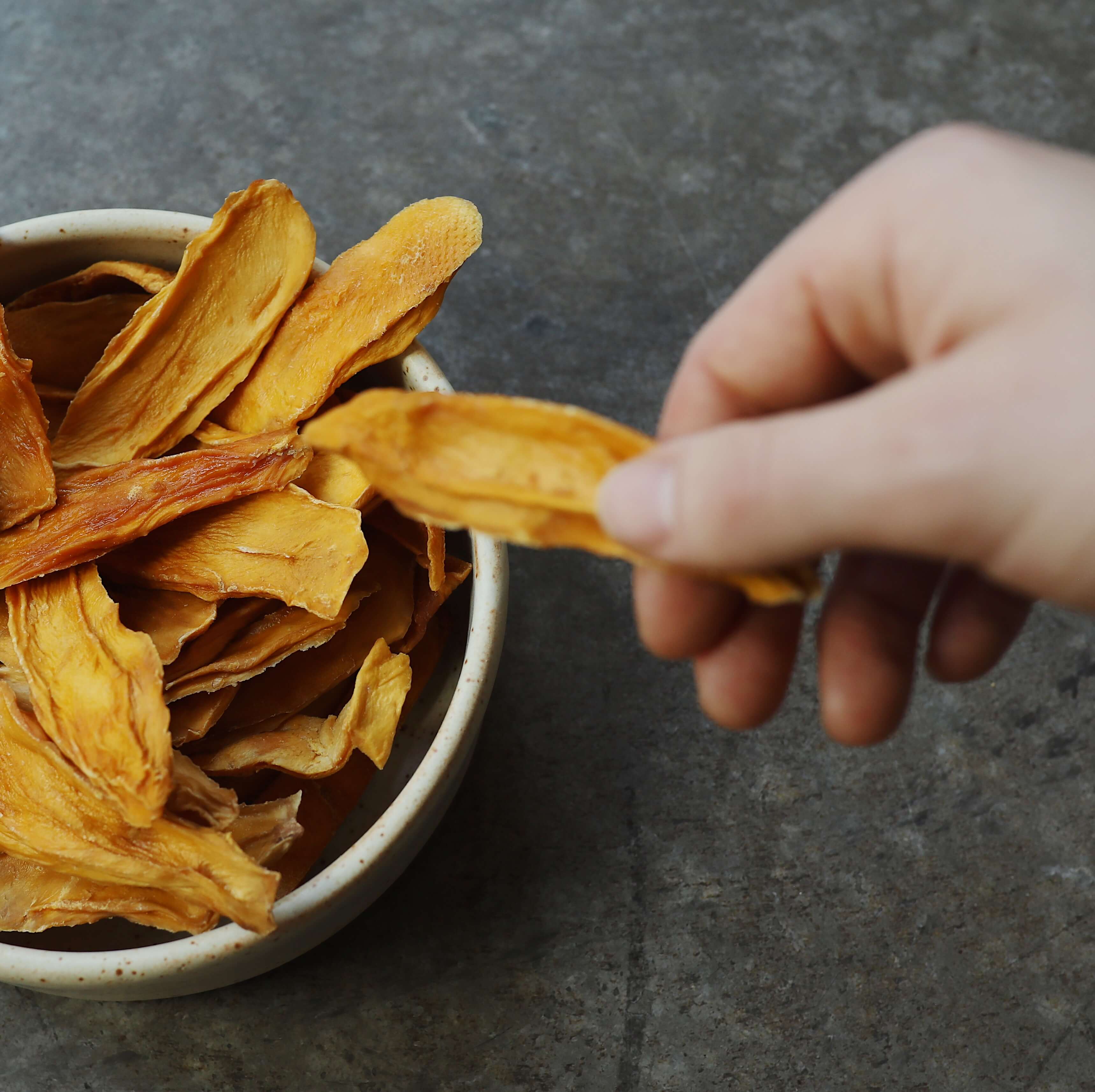 Hand reaching and grabbing an organic dried mango snack from a bowl.