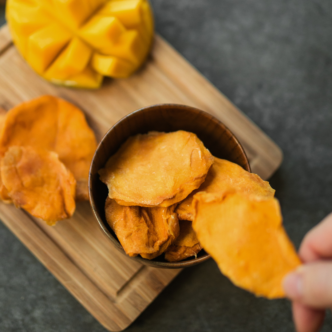 Hand picking up dried mango cheek from bowl, the perfect natural snack.